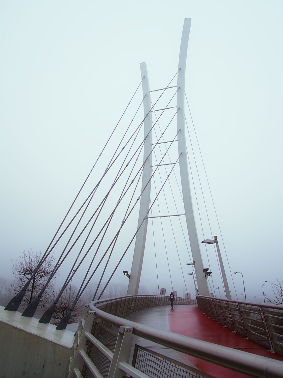 Kładka dla pieszych i rowerzystów we mgle, z samotną osobą przez nią przechodzącą.