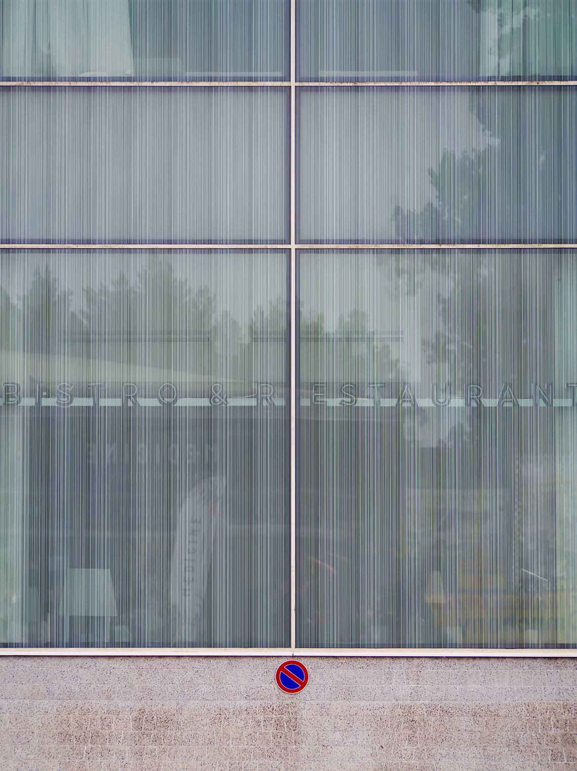 Sześćiodzielna szklana witryna. Pod witryną murek z małym znakiem drogowym zakaz postoju.