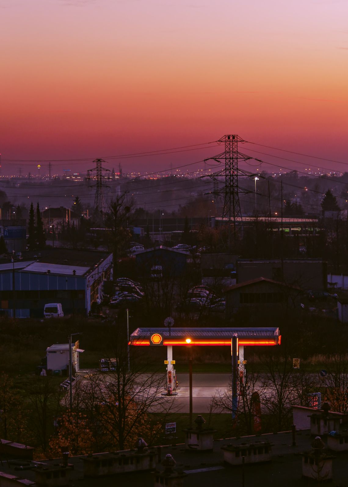 Zmierzch. Na pierwszym planie oświetlona stacja benzynowa. W tle budynki przemysłowe i słupy wysokiego napięcia.